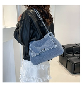 Detail of blue denim shoulder bag showing woven texture and silver chain strap