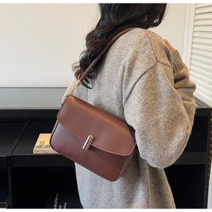 Brown leather square bag with silver metal buckle shown on a grey knitted sweater