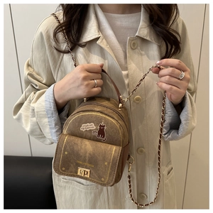 Détail d'un sac bandoulière marron vintage avec imprimé chat et chaîne sur un trench-coat