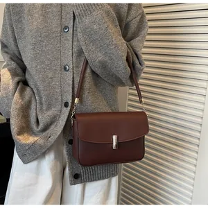 Detail of dark brown leather shoulder bag with silver buckle worn with a gray cardigan