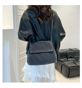 Detail of dark grey washed denim crossbody bag with silver chain strap on model