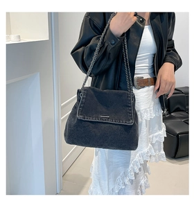 Detailed view of black denim crossbody bag with silver chain strap on model with leather jacket