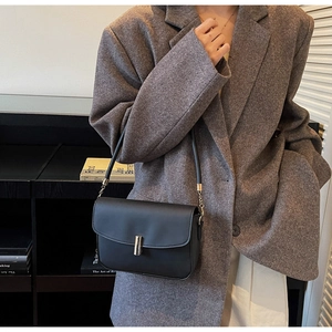 Detail of minimalist black leather shoulder bag with silver cylindrical metal buckle