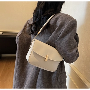 Close-up of elegant ivory shoulder bag with a gold T-shaped buckle and chain strap detail