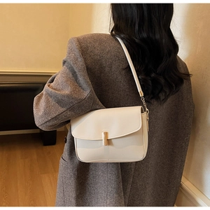 Detail of a creamy white crossbody bag featuring a sleek gold cylindrical metal buckle