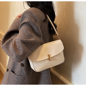 Side view of white crossbody bag with gold lock and thin shoulder strap on model