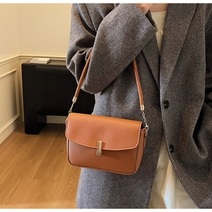 Brown leather crossbody bag with gold buckle detail worn with a grey wool coat