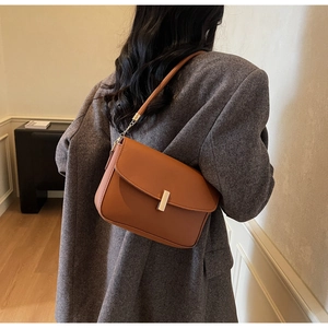Brown leather underarm bag with gold lock shown on model wearing grey blazer