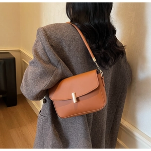 Detail of caramel brown leather shoulder bag with gold metal clasp on gray suit
