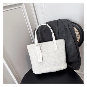 Detail of white teddy fleece tote bag with leather handles on a minimalist chair