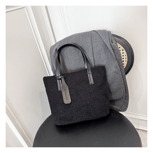 Detail of black faux shearling tote bag featuring leather handles and fashion logo tag