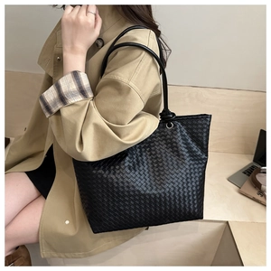 Detail of black woven tote bag featuring intricate knot design and spacious leather texture