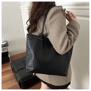 Detail of large woven black tote bag with metal ring handles on brown blazer outfit
