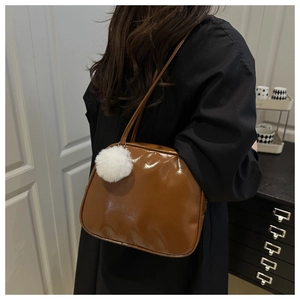 Caramel patent leather shoulder bag detail with a white plush pom-pom keychain accessory