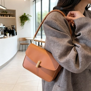 Minimalist caramel leather flap shoulder bag with gold metal clasp on model