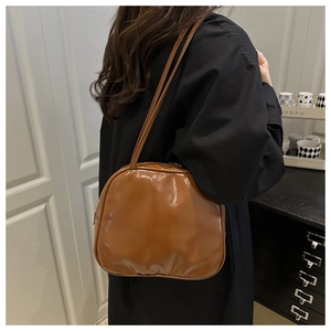 Brown faux leather shoulder bag with glossy finish shown on model in home setting