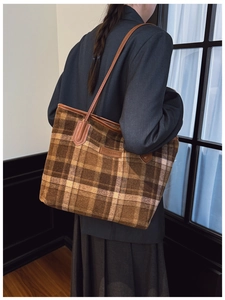 Detail of a large brown plaid tote bag in wool fabric worn on shoulder by a model