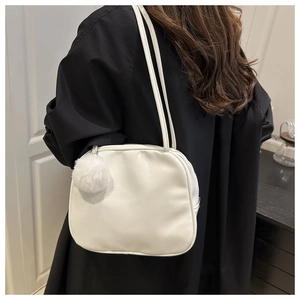 Close-up of a white leather shoulder bag with a soft pom-pom charm and slim straps