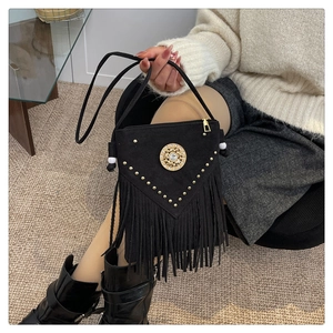 Detail of black suede crossbody bag with long fringes, gold studs and metal ornament