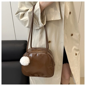 Close-up of brown glossy PU leather travel toiletry bag with white plush ball charm detail