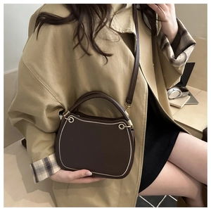 Detail of dark brown saddle bag with golden hardware rings and contrast stitching accents