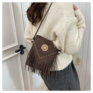 Detail of brown suede crossbody bag featuring gold rivets, fringes and bead strap decor