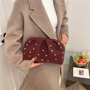 Fashionable burgundy velvet clutch bag with golden rivets shown in a lifestyle setting