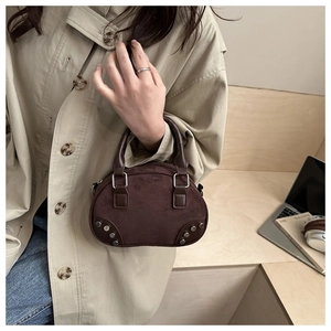 Detail view of dark brown suede shell bag with silver rivets held by a model