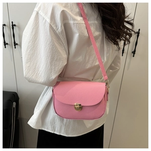 Close-up of pink lychee leather saddle bag with gold metal lock on white shirt model