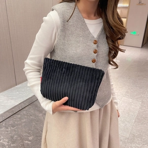 Close-up of black corduroy clutch bag featuring red fashion label in high-end texture