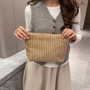 Detail of light brown corduroy textured clutch bag with vertical stripe pattern and side tag