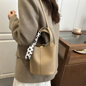 Chic camel leather bucket bag with polka dot scarf detail on minimalist home background