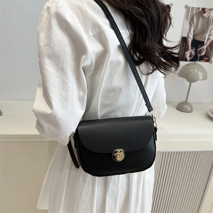 Minimalist black pebble leather saddle bag for women with gold clasp worn by model