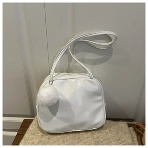 Close-up of white glossy patent leather handbag with a plush fur ball charm on knit mat