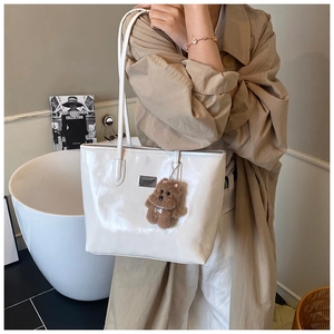 Glossy cream tote bag with stylish teddy bear charm and polished metallic logo detail