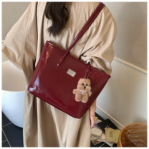 Detail of burgundy patent leather tote bag with metallic plaque and plush bear charm