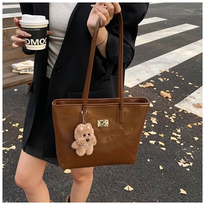 Brown faux leather tote bag with gold hardware and plush dog pendant in street style