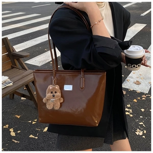 Close-up of brown glossy leather tote bag with silver plaque and plush bear charm decoration
