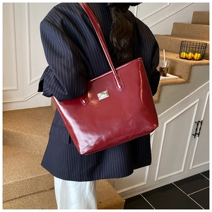 Detailed view of glossy burgundy patent leather tote bag on model in a stylish suit