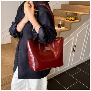 Close-up of a burgundy patent leather tote bag styled with a striped navy blazer and white pants