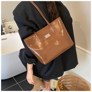 Detail of glossy brown patent leather tote bag with silver metal plaque on the front