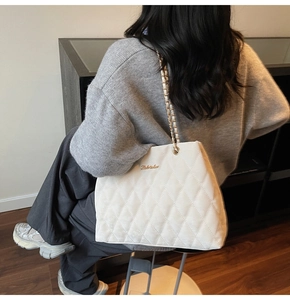 Detail of cream quilted tote bag featuring gold chain straps and textured rhombus stitching