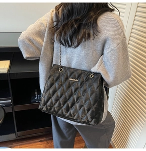 Close-up of black quilted shoulder bag with gold chain strap worn by a female model