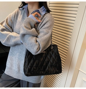 Detail of black quilted leather shoulder bag with metal chain strap and logo