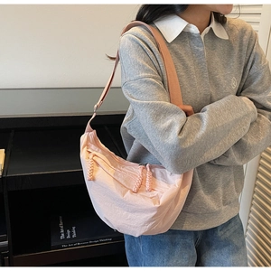 Detail of light pink nylon crescent bag featuring smooth texture and braided zipper pulls