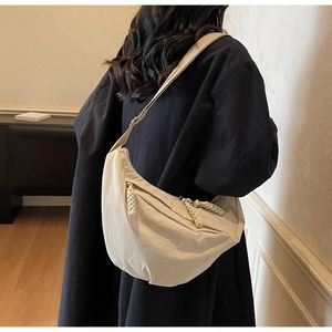 Close-up of a beige crescent shoulder bag with pleated texture and woven zippers