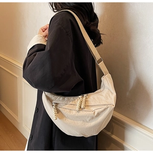 Detail of off-white crescent crossbody bag with woven zipper pull and wide strap