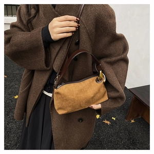 Détail d'un sac Boston en daim marron avec poignées en cuir porté par un mannequin de profil