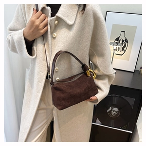 Détail du sac baguette en daim marron foncé avec boucles dorées sur un manteau beige