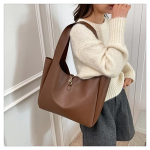 Detailed close-up of a large brown leather tote bag with a golden lobster clasp detail